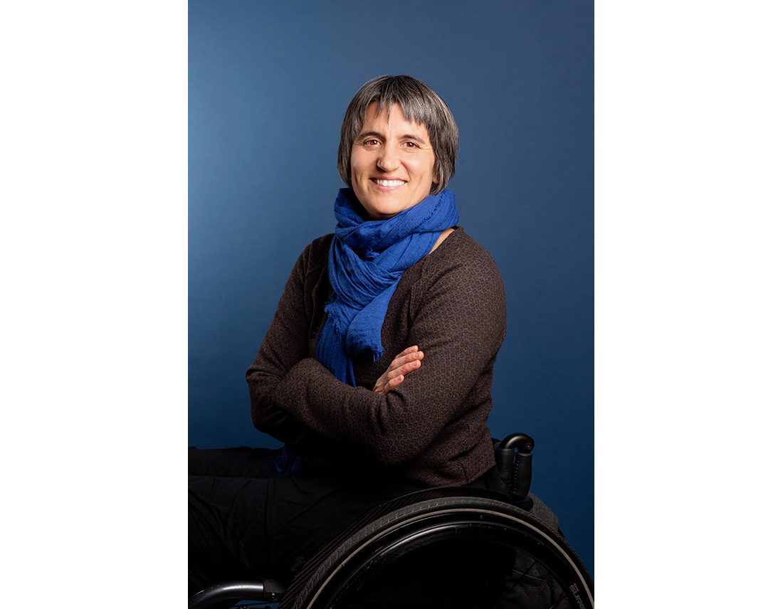 Portrait de Emmanuelle Assmann en fauteuil roulant sur fond bleu, handicap, style corporate