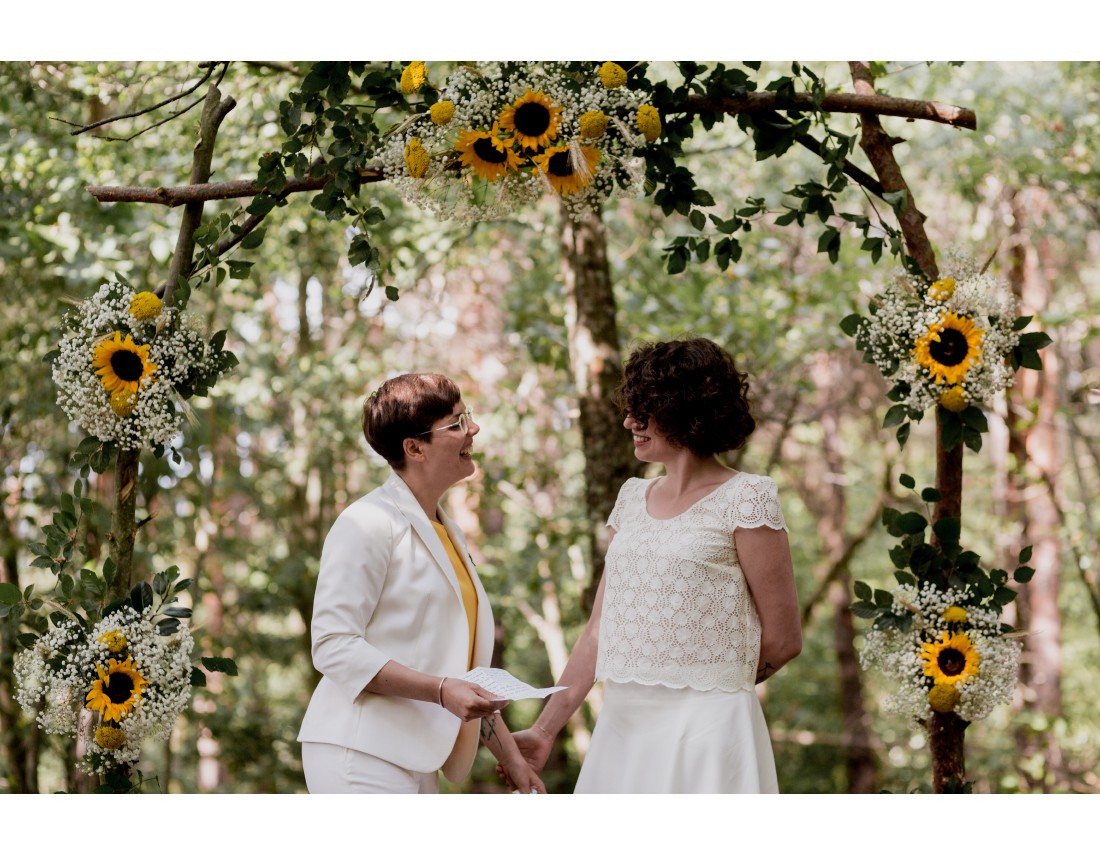 Echange de voeux sous l'arche fleurie de tournesol pendant ceremonie laique de mariage lesbien.