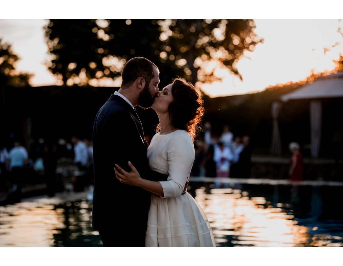 Couple de mariés qui s'embrasse au coucher de soleil devant la piscine du chateau de courban.